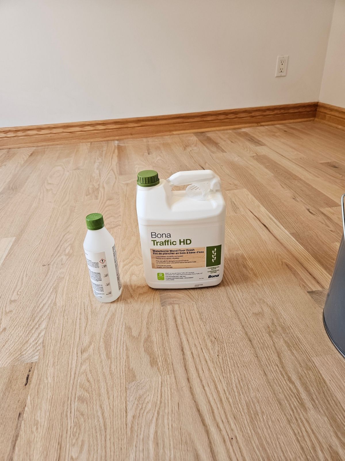 Un gallon de liquide est posé sur un plancher en bois à côté d'une bouteille plus petite.
