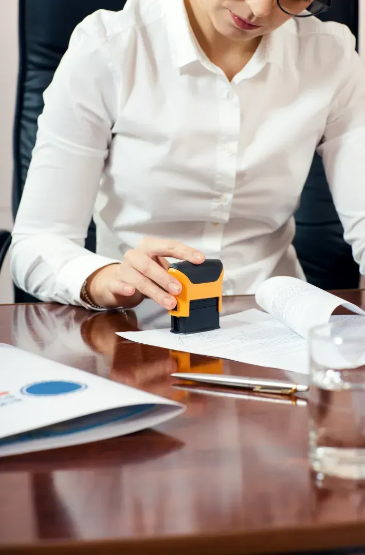 Woman in white shirt stamping paperwork at a desk.