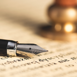 Fountain pen on old paper with inkwell blurred in the background.