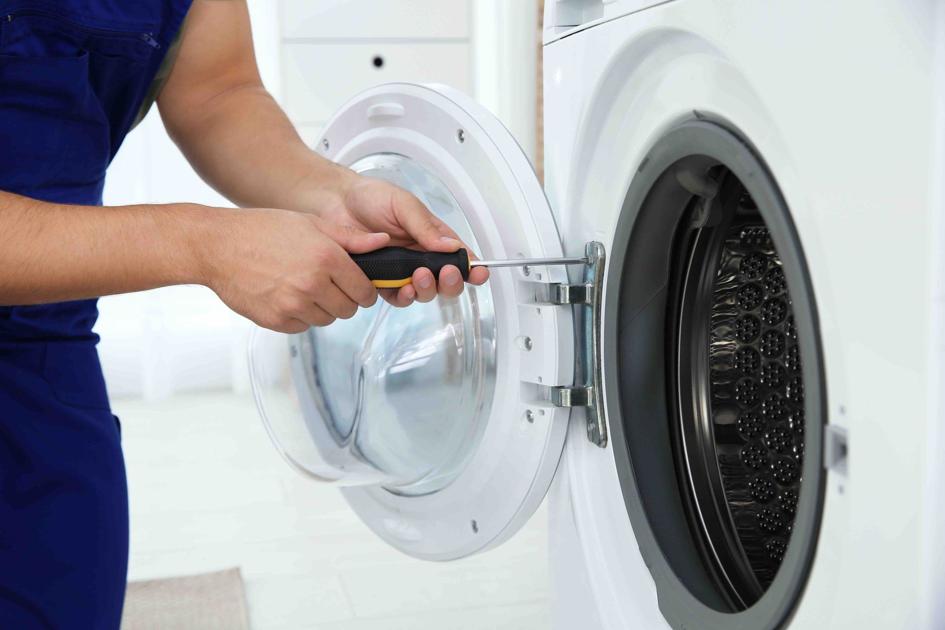 Technician using a screwdriver to repair an open washing machine door