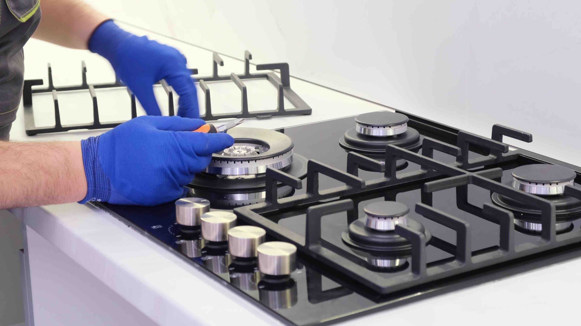 Gloved hands adjusting a gas stove burner in a kitchen with black grates and silver knobs