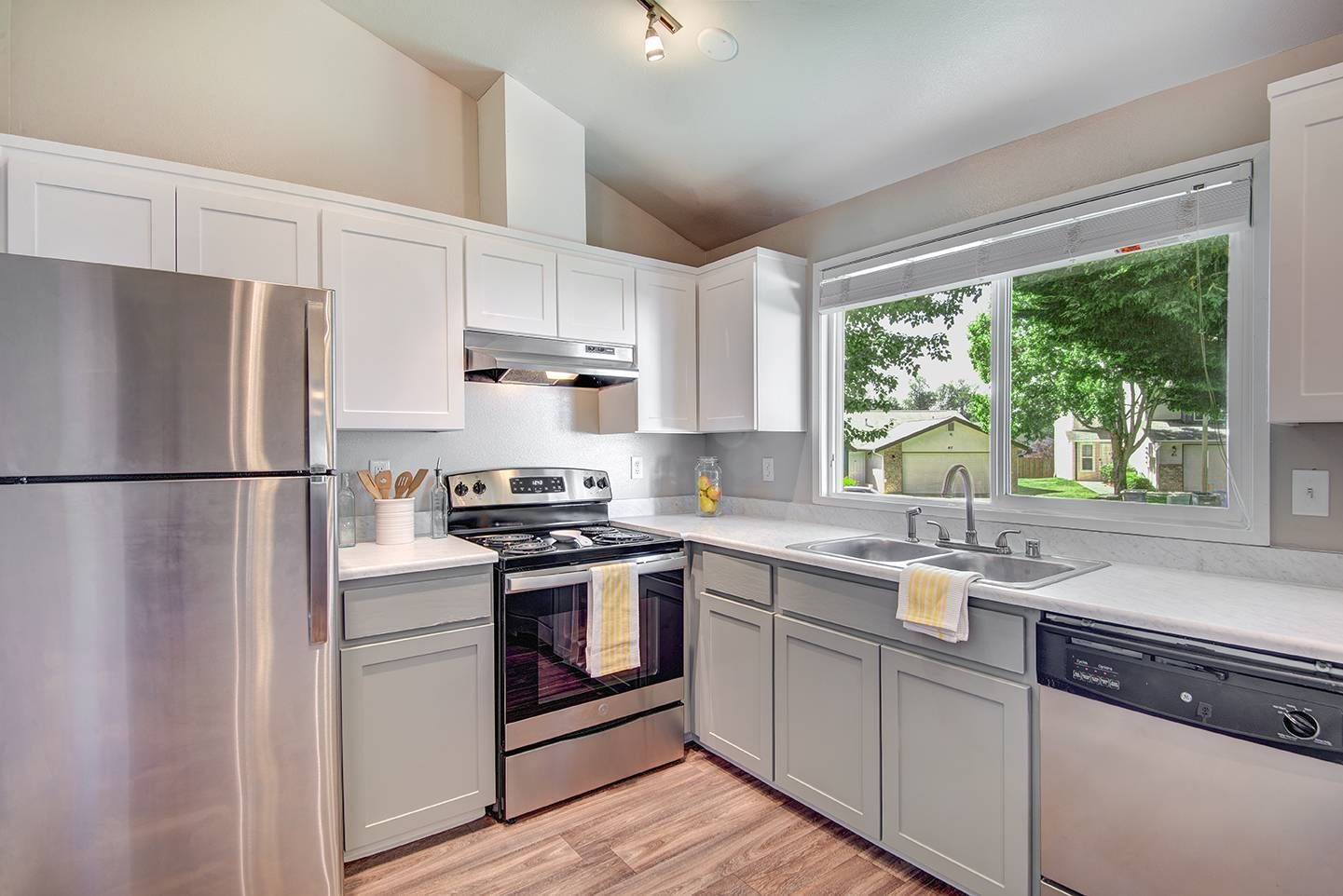 Modern kitchen with stainless steel appliances, light gray cabinets, and a large window.