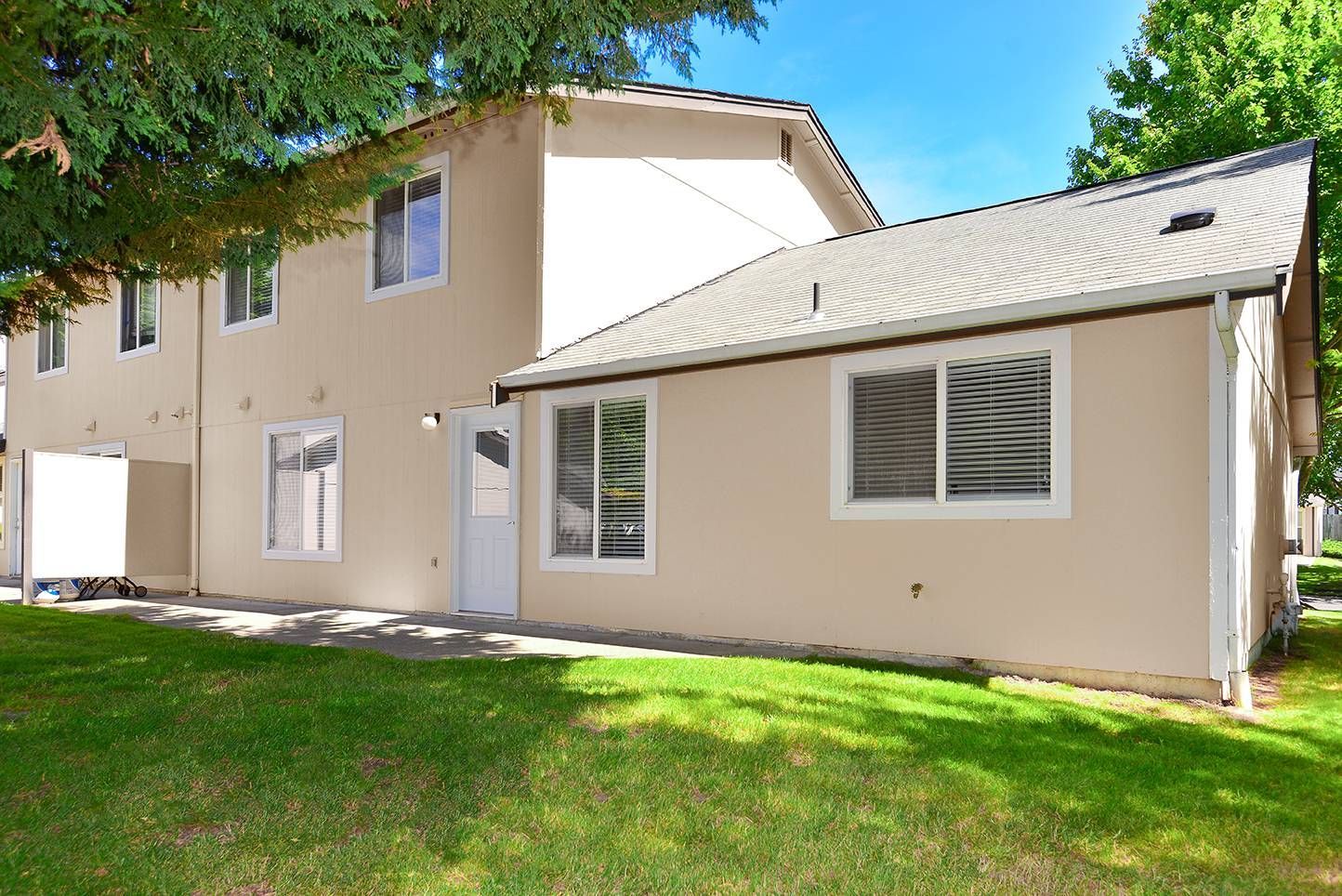 Beige two-story apartment building with white-trimmed windows and green lawn.
