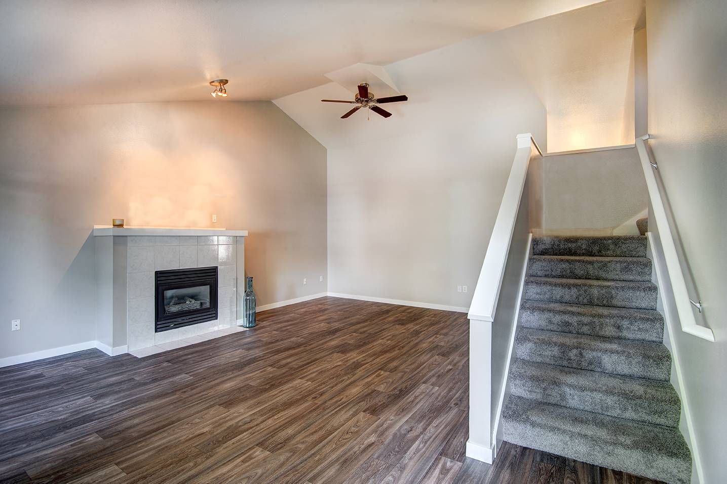 Living room with a gas fireplace, ceiling fan, wood-look flooring, and carpeted stairs.