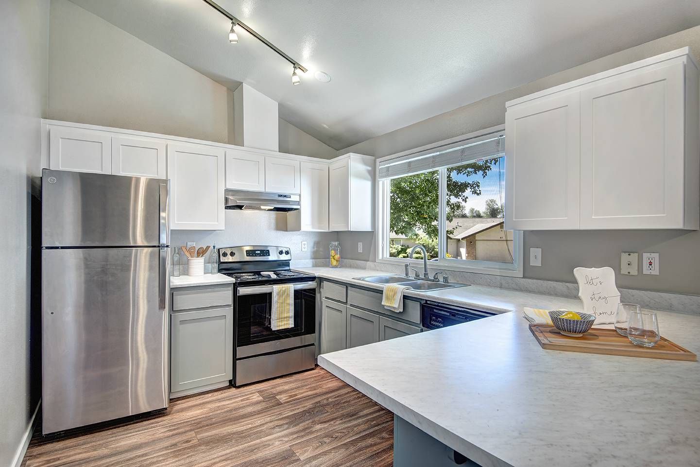 Bright kitchen with white cabinets, stainless steel fridge and stove, and a large window.