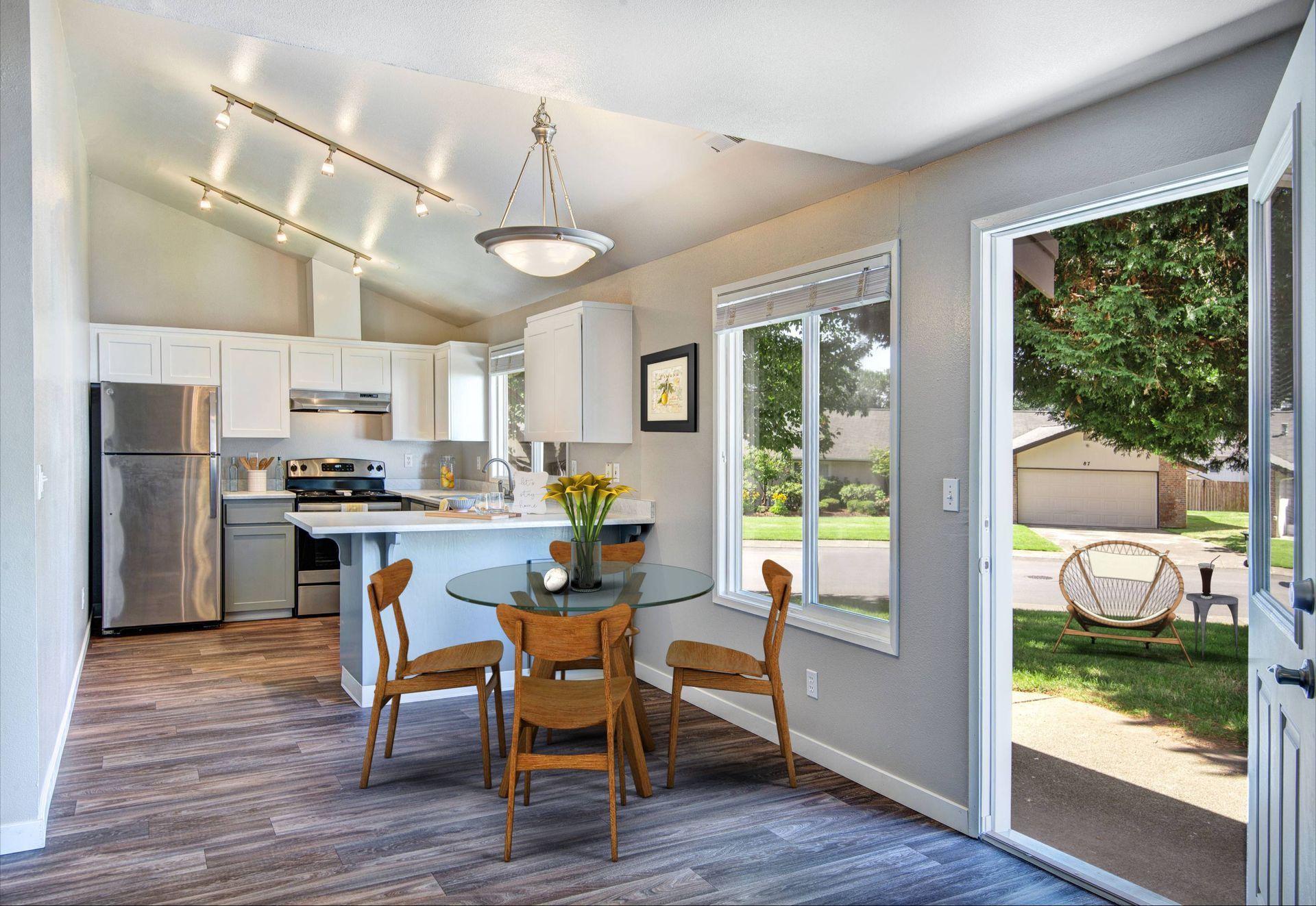 Bright apartment kitchen and dining area with white cabinets, stainless appliances, island, glass round table, and a door to the outdoors.