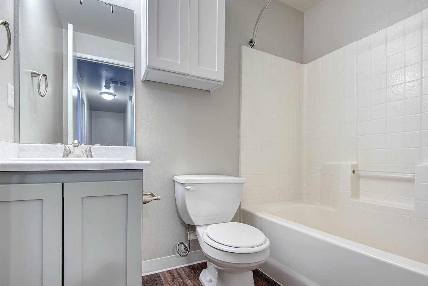 Bathroom with a gray vanity, mirror, toilet, and white-tiled tub/shower.