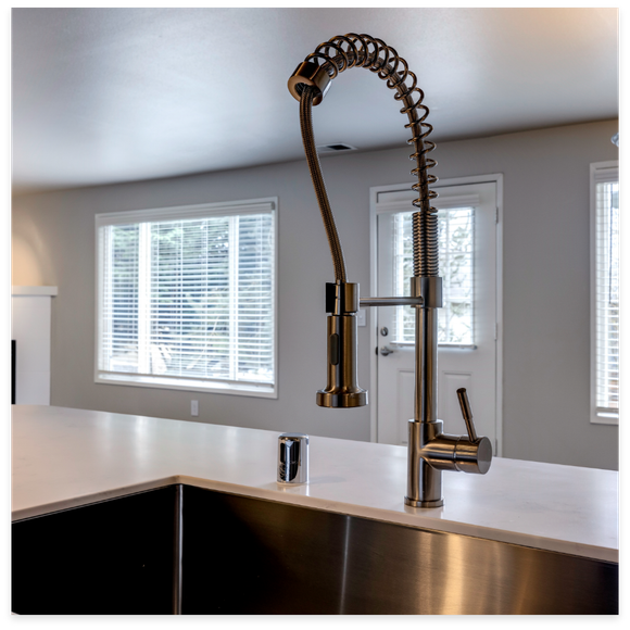 Stainless steel kitchen faucet with pull-down sprayer, installed on a white countertop.