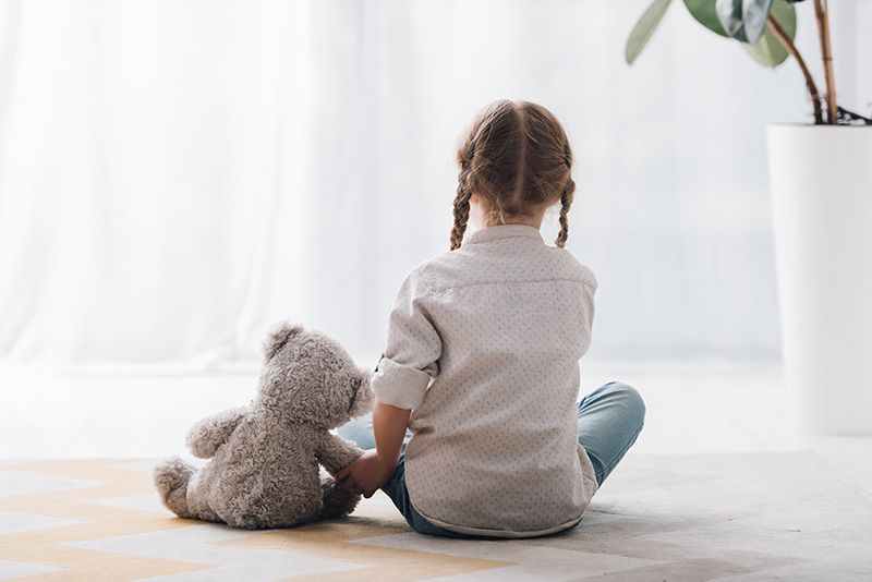 Sad kid with Teddy bear looking out window