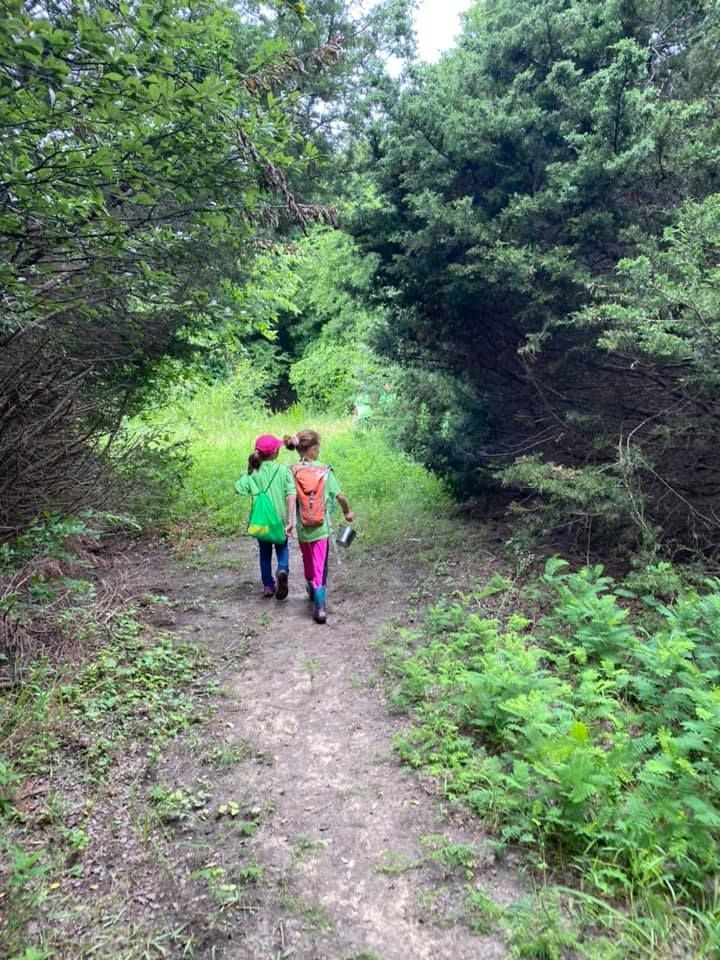 Two children walking along a wooded trail under a green tree canopy