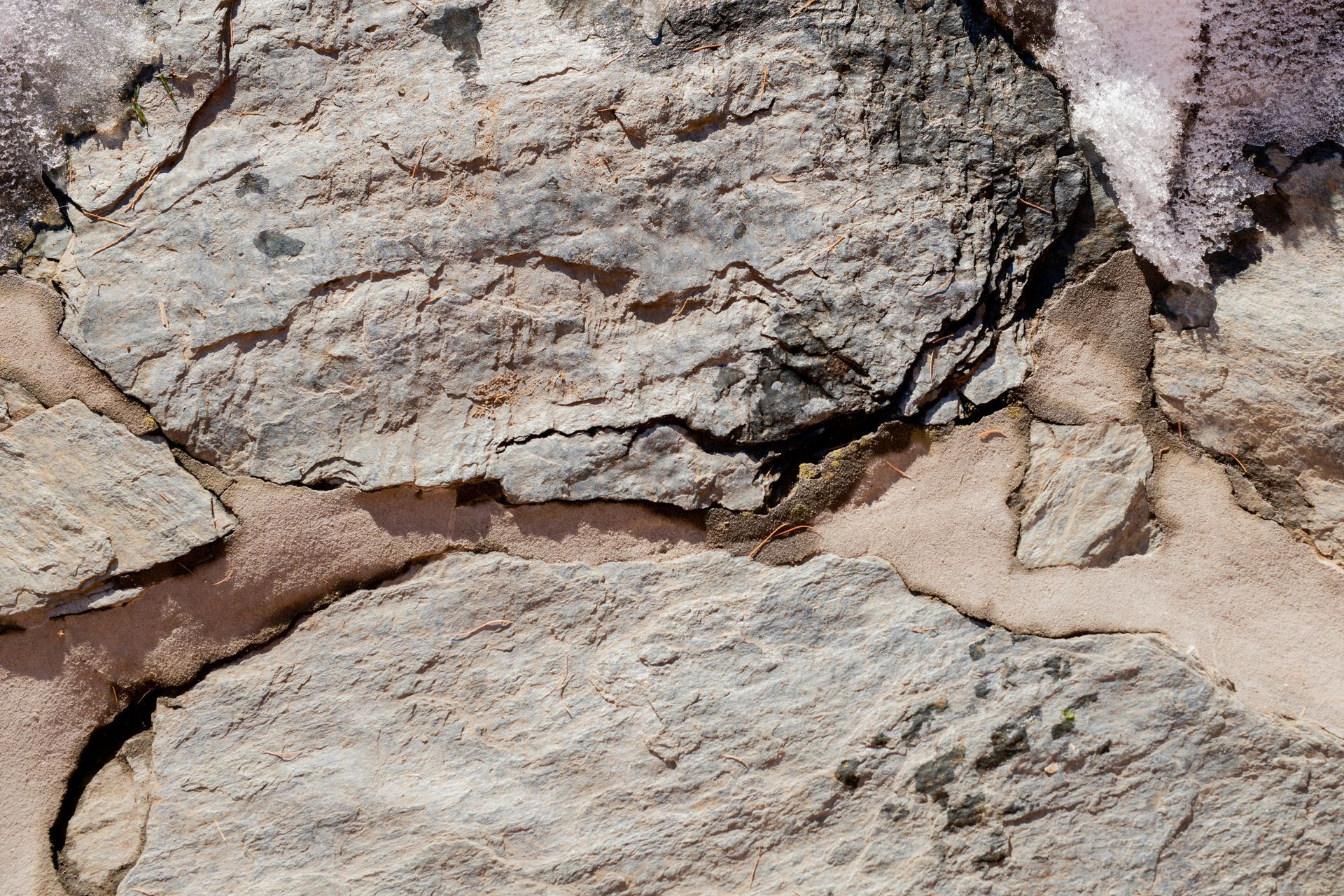 Close-up of a weathered stone wall with irregular tan, gray, and purple stones joined by tan mortar.