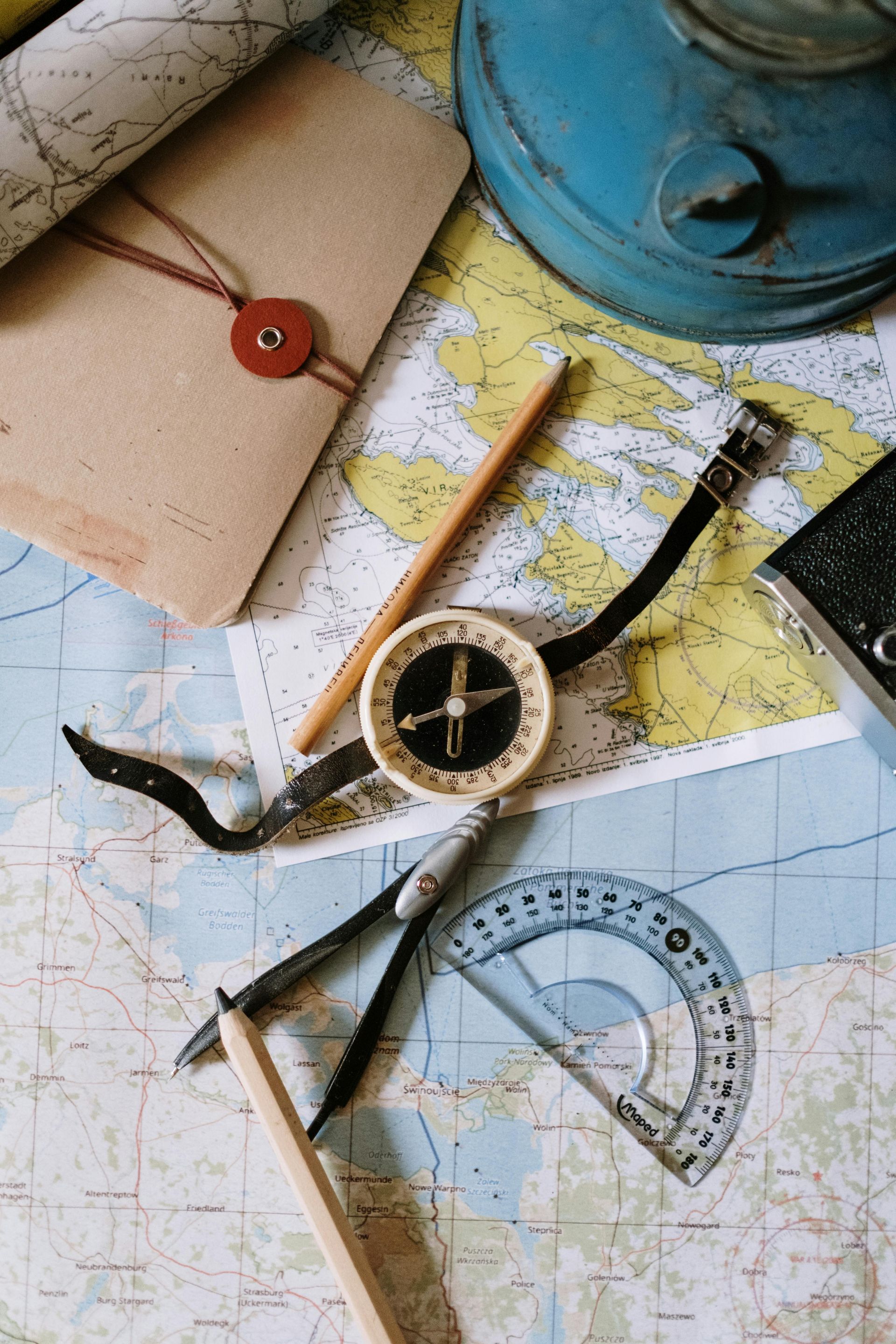 Maps, compass, protractor, and other navigation tools laid on a table.