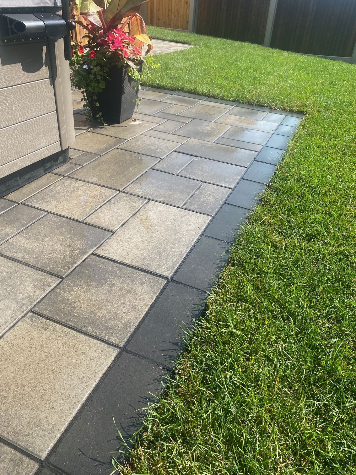 a patio with a black border and a lush green lawn .