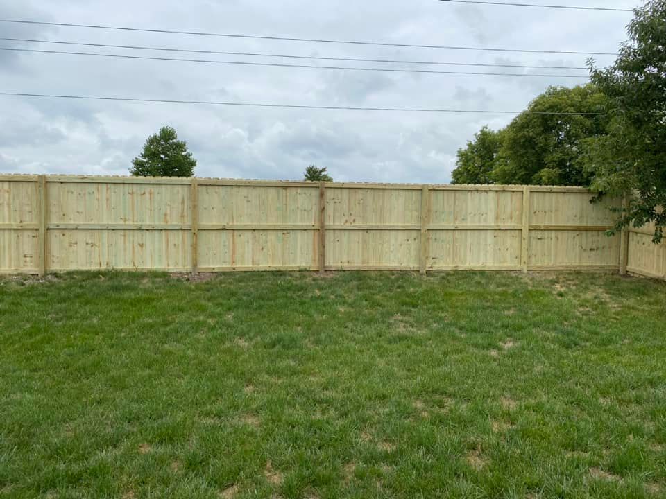 Grassy backyard with a tall light wood privacy fence under a cloudy sky