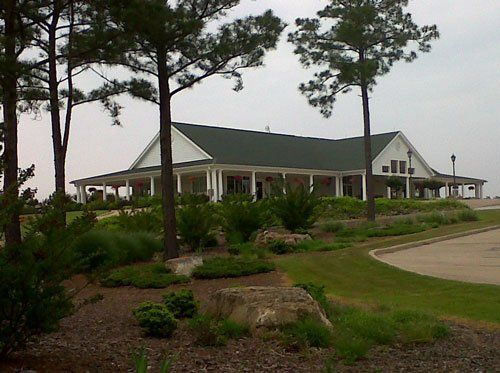 A white house with a green roof is surrounded by trees