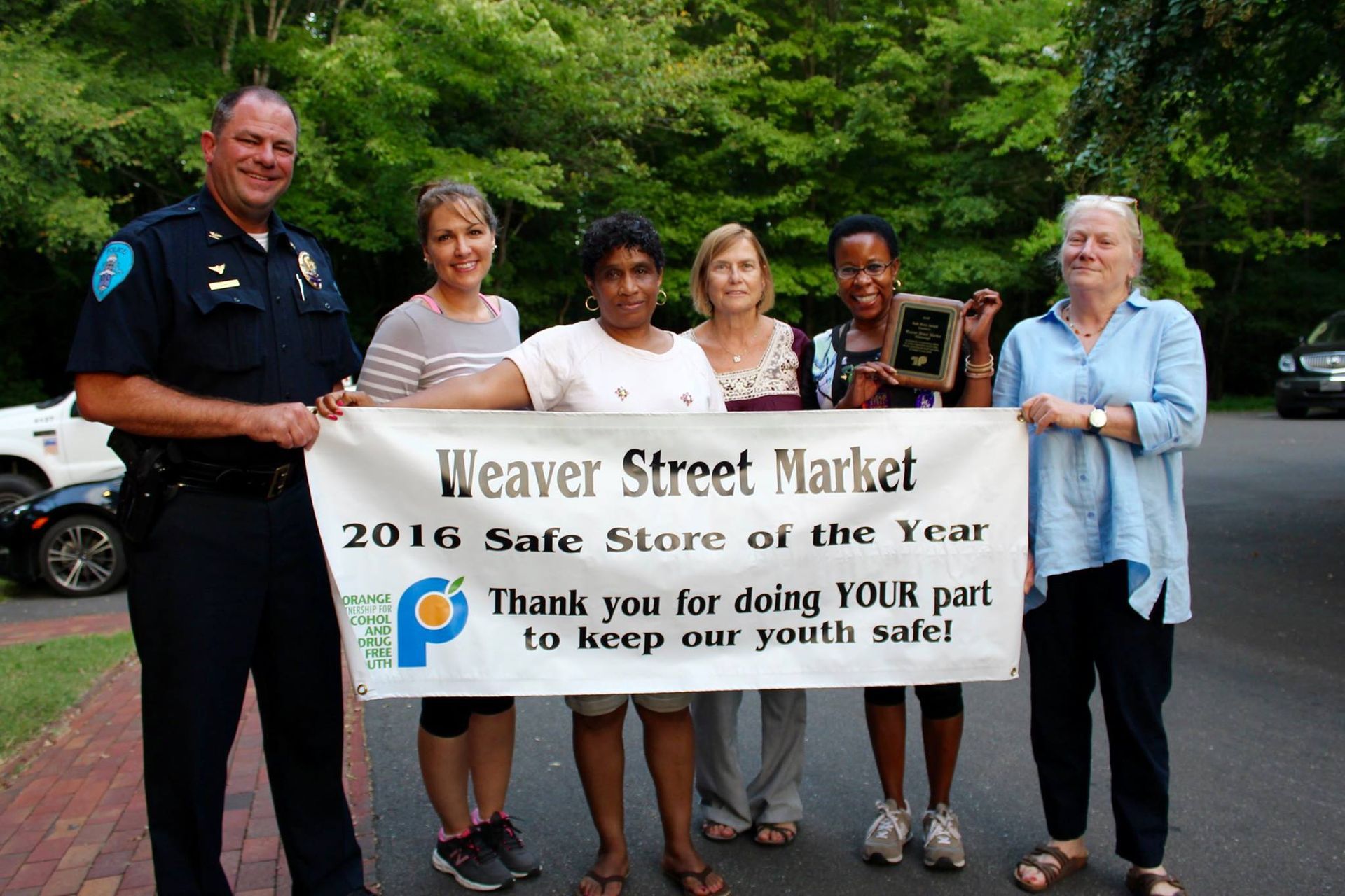 A group of people holding a weaver street market banner