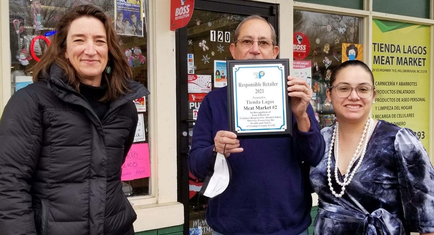 Three people standing in front of a store holding a certificate