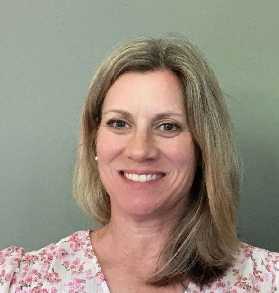 A woman wearing a black sweater and a red shirt is smiling for the camera.