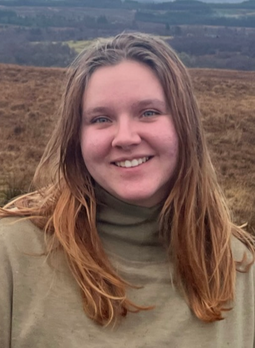 A woman wearing a black sweater and a red shirt is smiling for the camera.