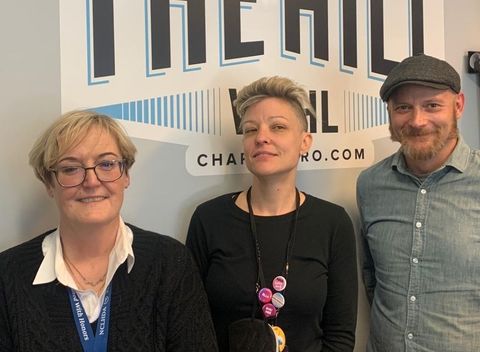 Three people standing in front of a sign that says the hill