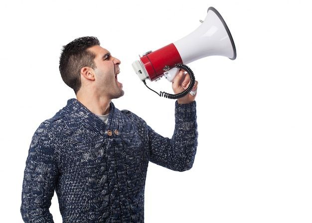 A man in a blue sweater is shouting into a red and white megaphone.