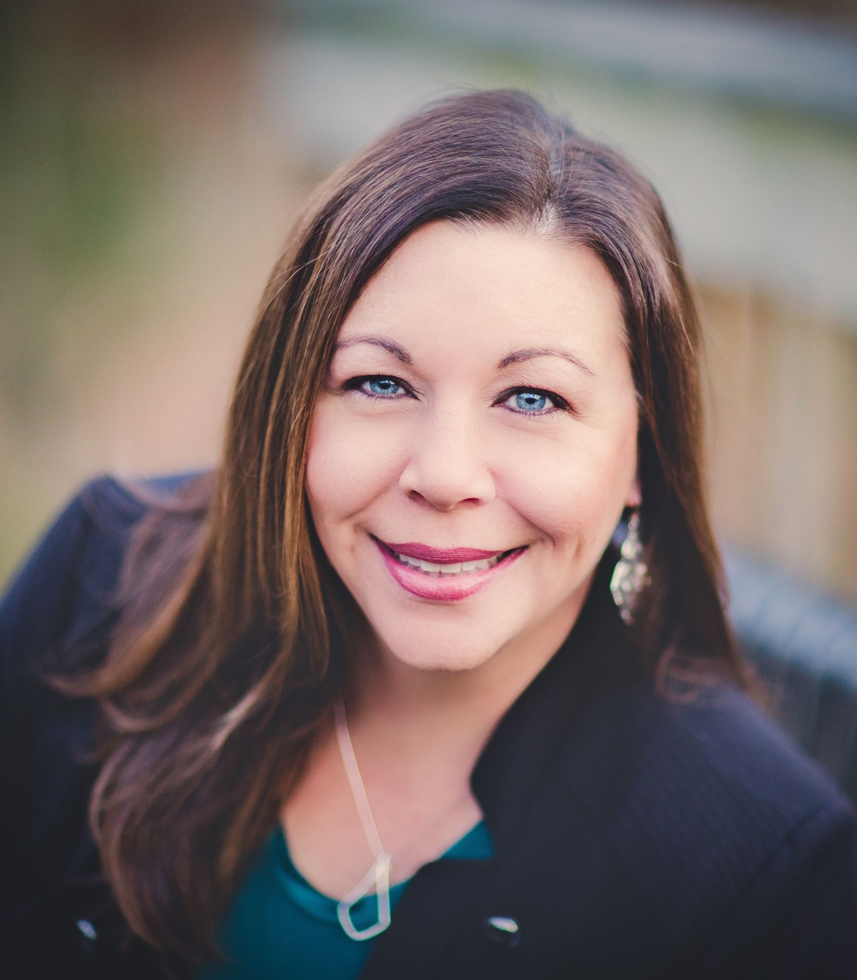 A woman wearing a black jacket and a green shirt smiles for the camera