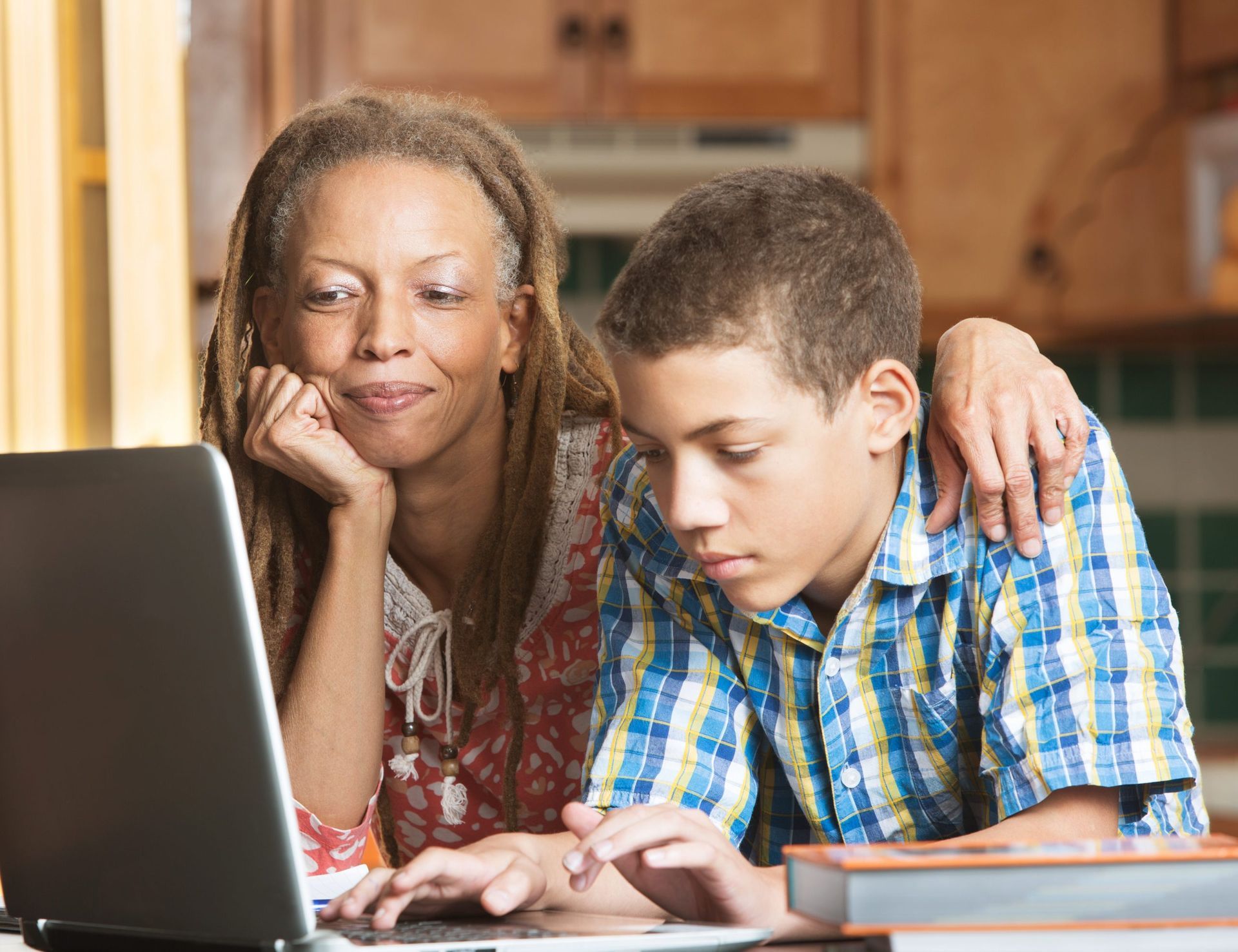 A woman and a boy are looking at a laptop together