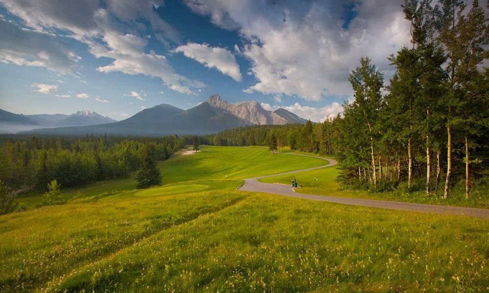 A road going through a grassy field with mountains in the background.