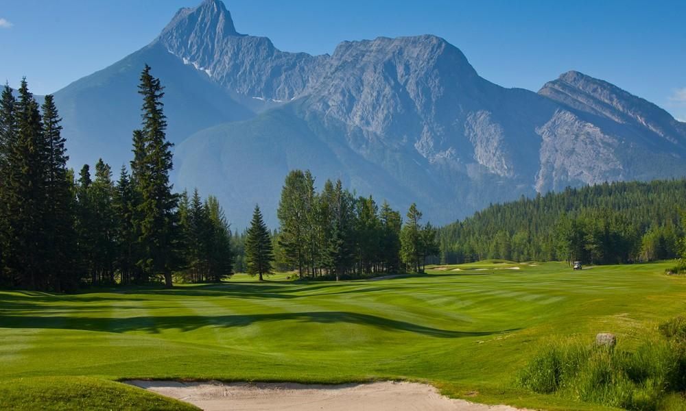 A golf course with mountains in the background and trees in the foreground.