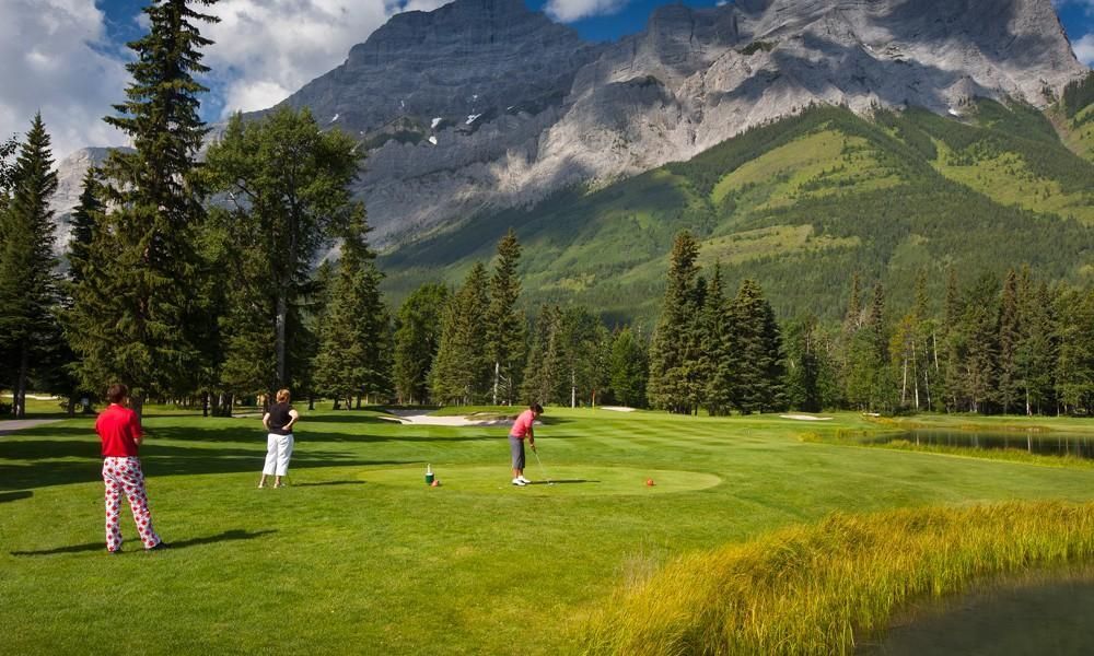Two people are playing golf on a golf course with mountains in the background.
