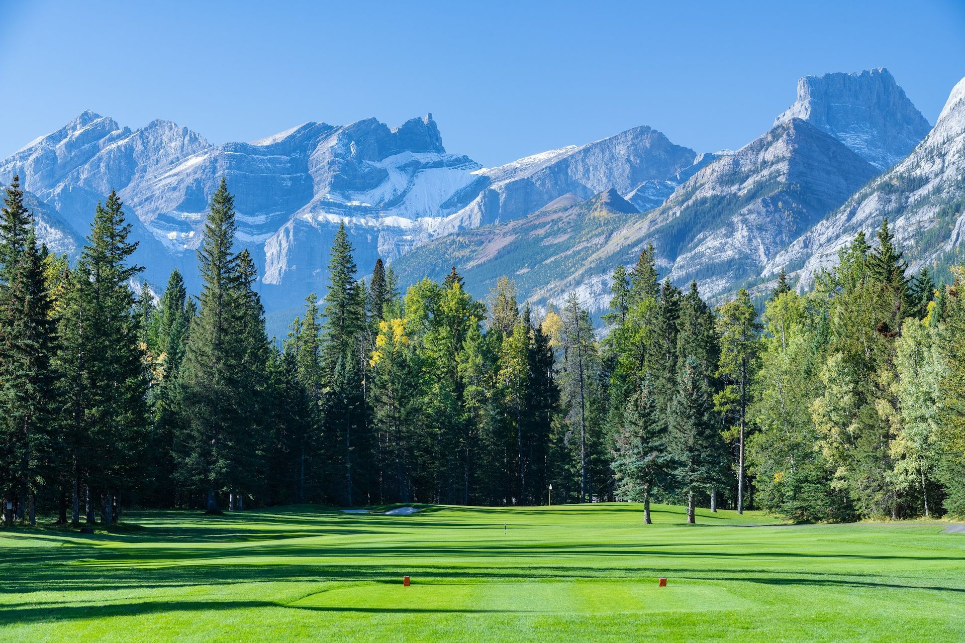 A golf course with mountains in the background and trees in the foreground.