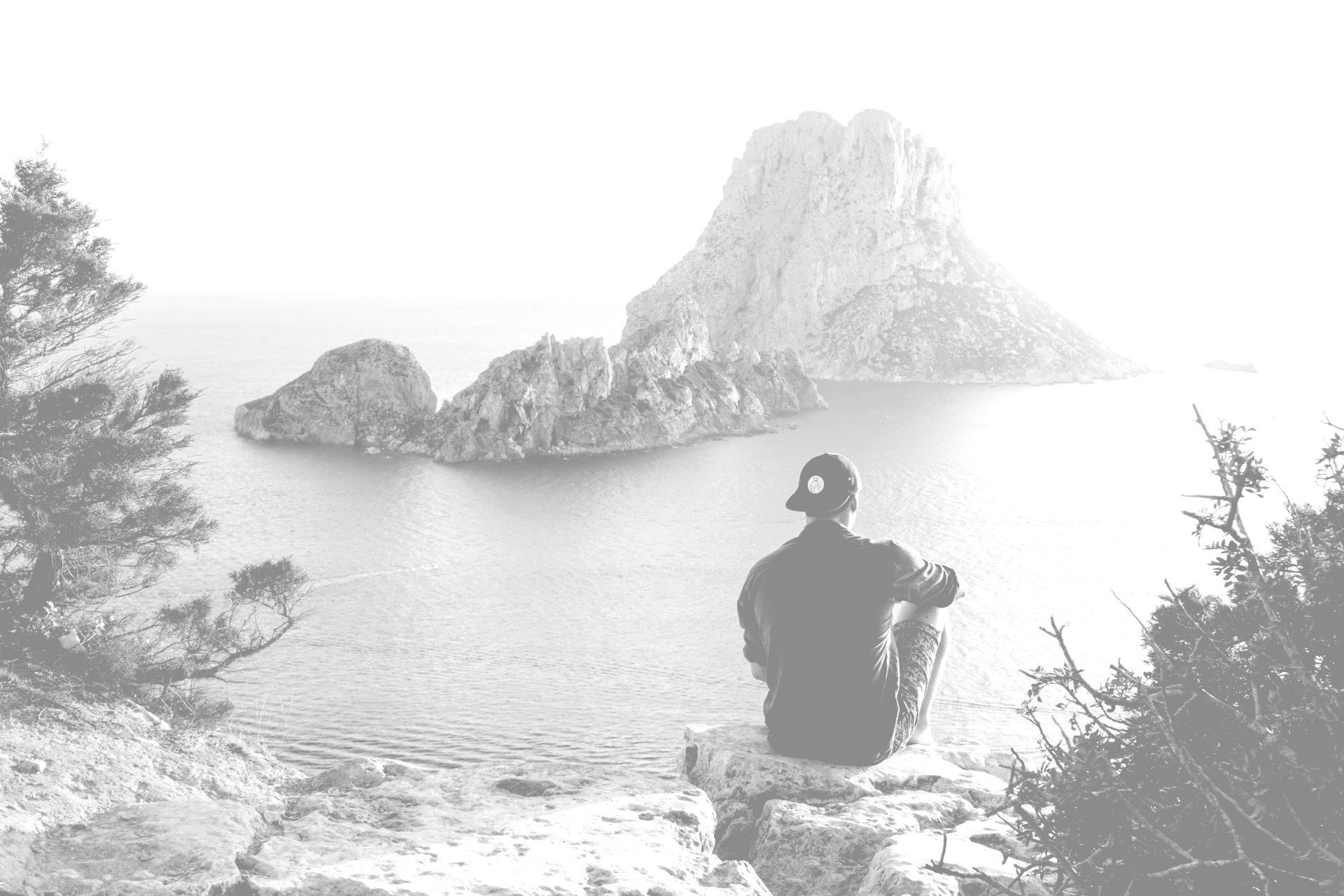 A man is sitting on a rock overlooking the ocean.