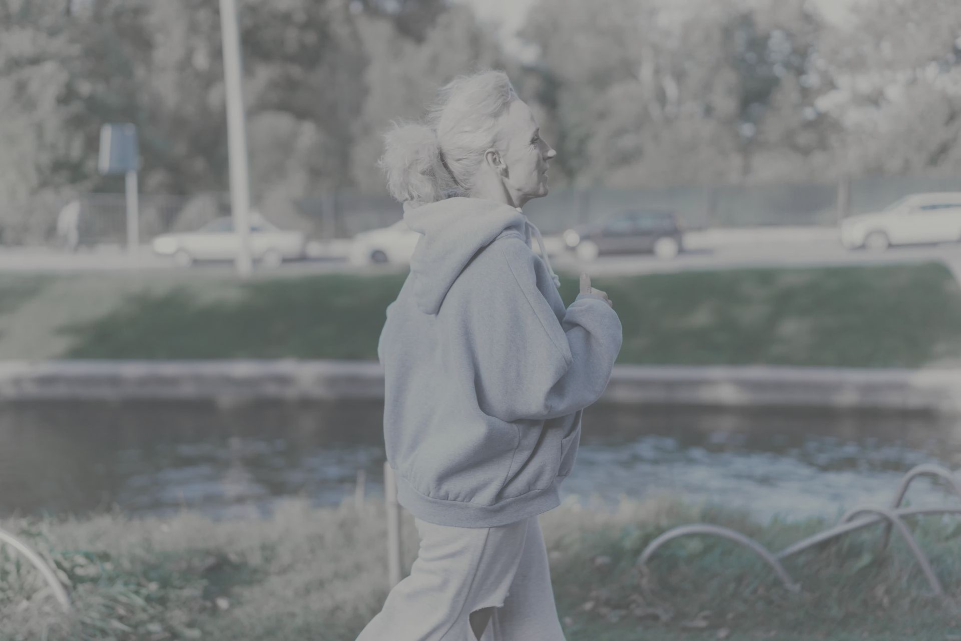 An elderly woman is jogging in a park near a river.