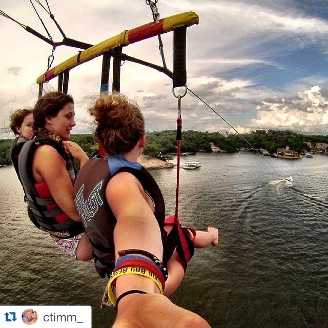 Two people parasailing over water with a shoreline and cloudy sky in the background