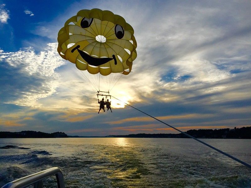 Parasailing over a sunset-lit ocean, with a yellow parachute and boat wake below