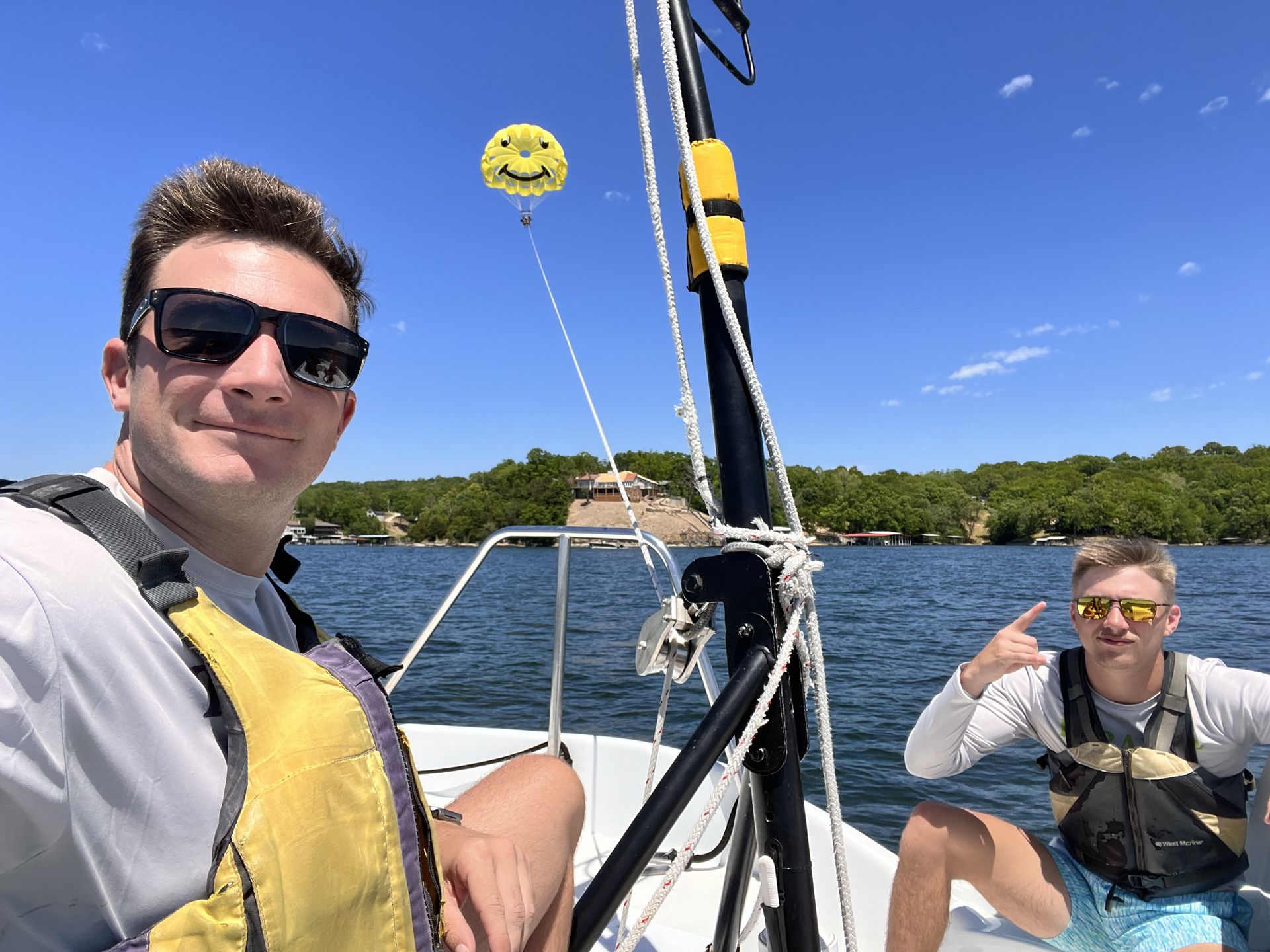 Two people on a sailboat, smiling on the water under a blue sky, with a smiley face balloon above.