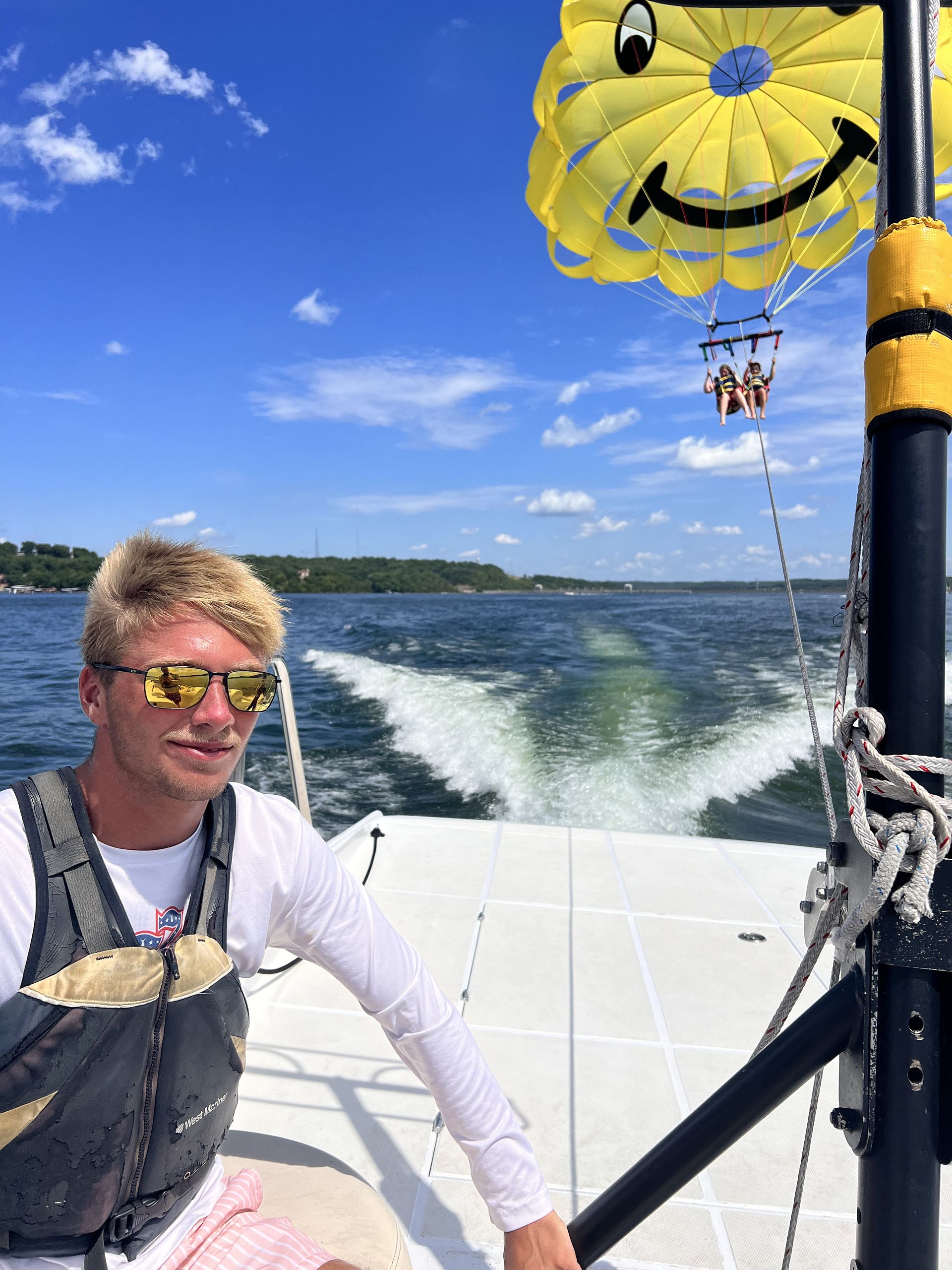 Man on a boat smiling beside a yellow parasail over the water