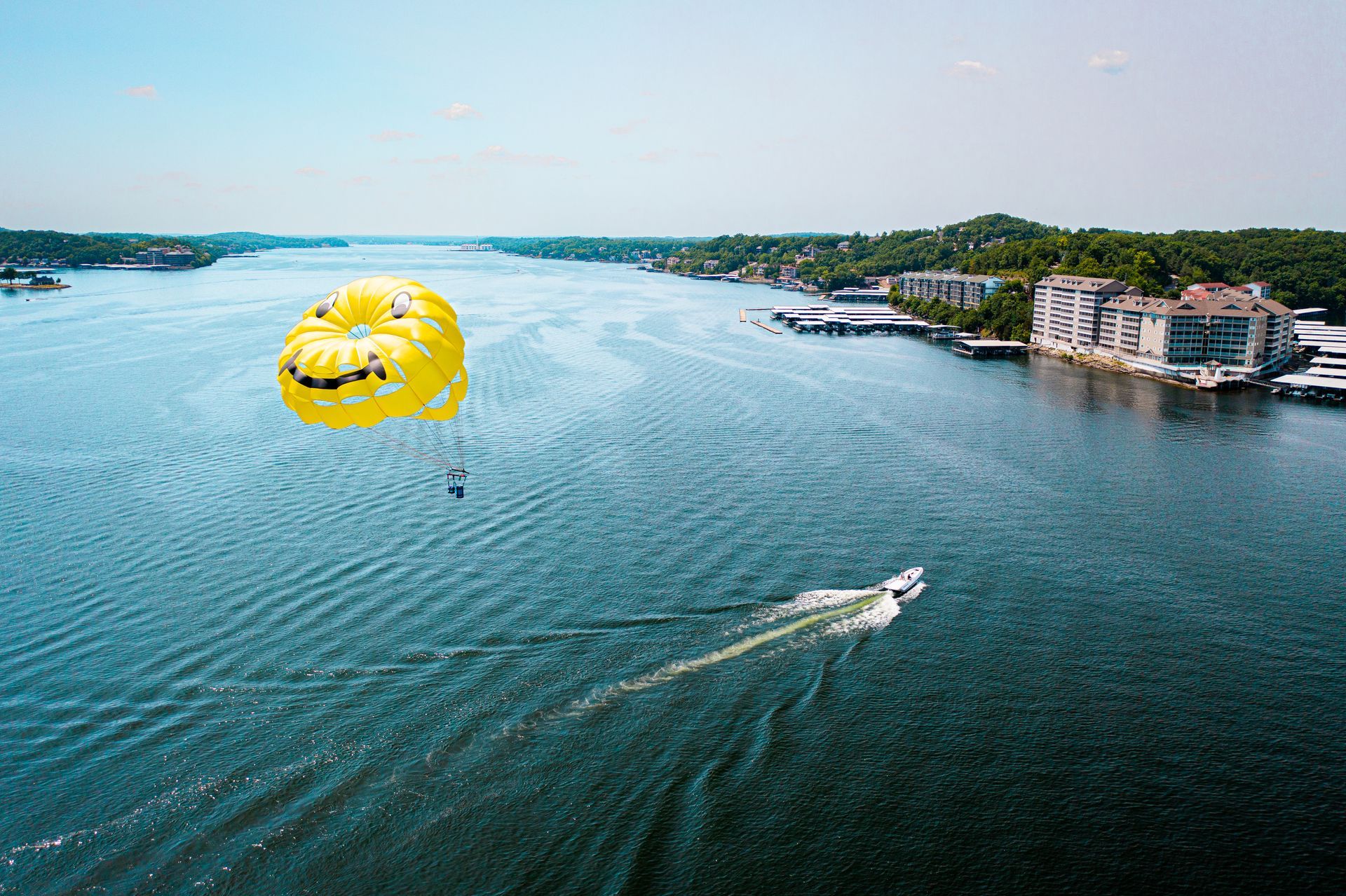 Yellow parasail over blue water with a speedboat towing it near a rocky shoreline