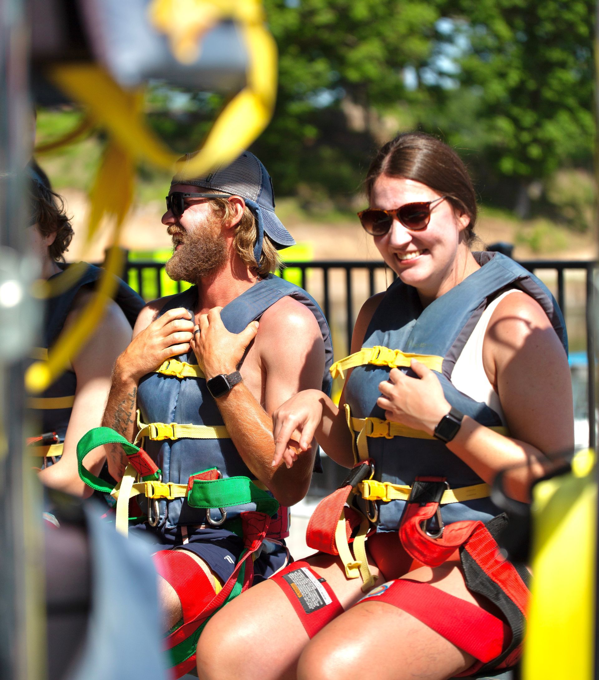 Two climbers in harnesses and helmets smile while seated on a ropes course outdoors