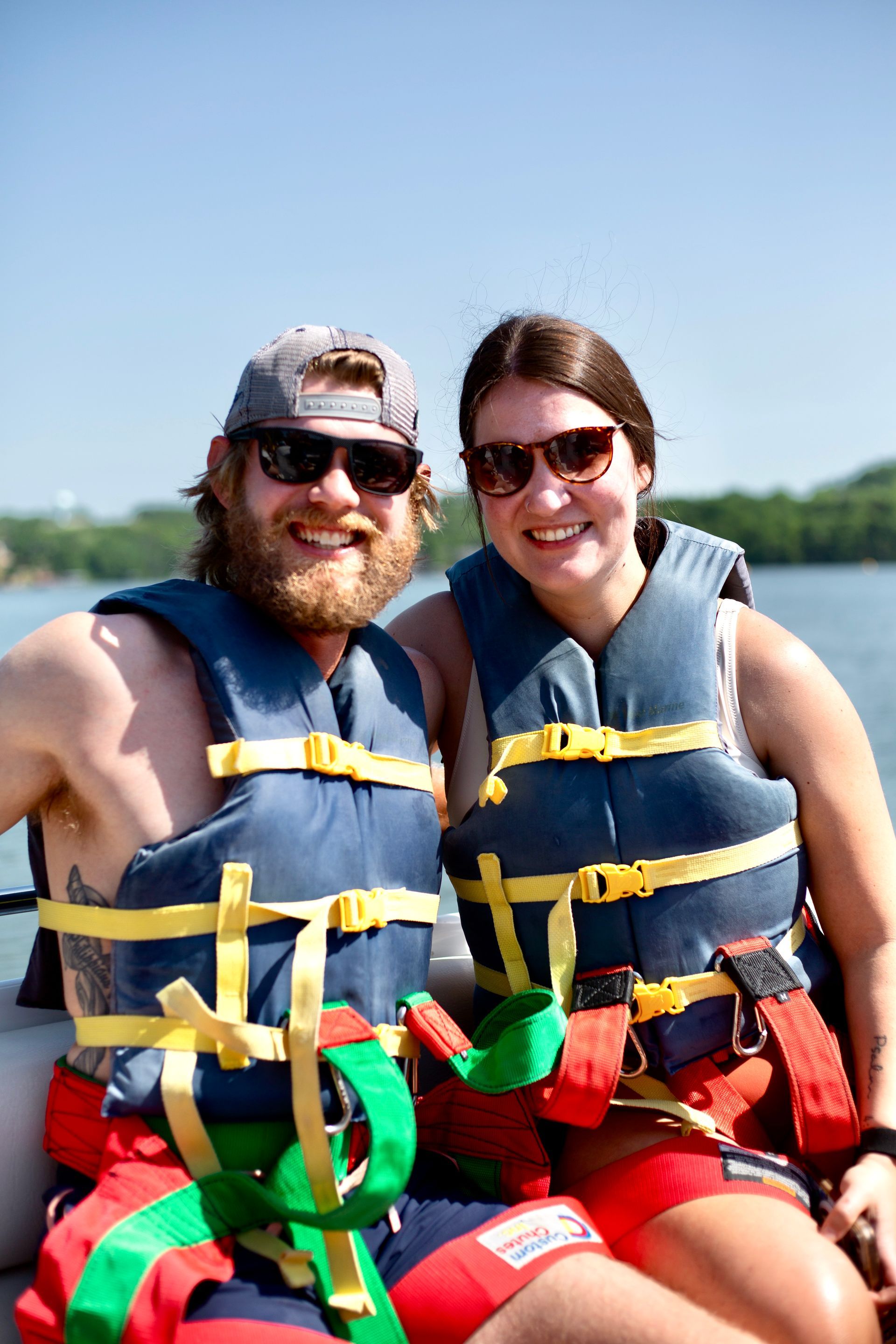 Two people wearing life jackets sit together on a boat, smiling on a sunny day.