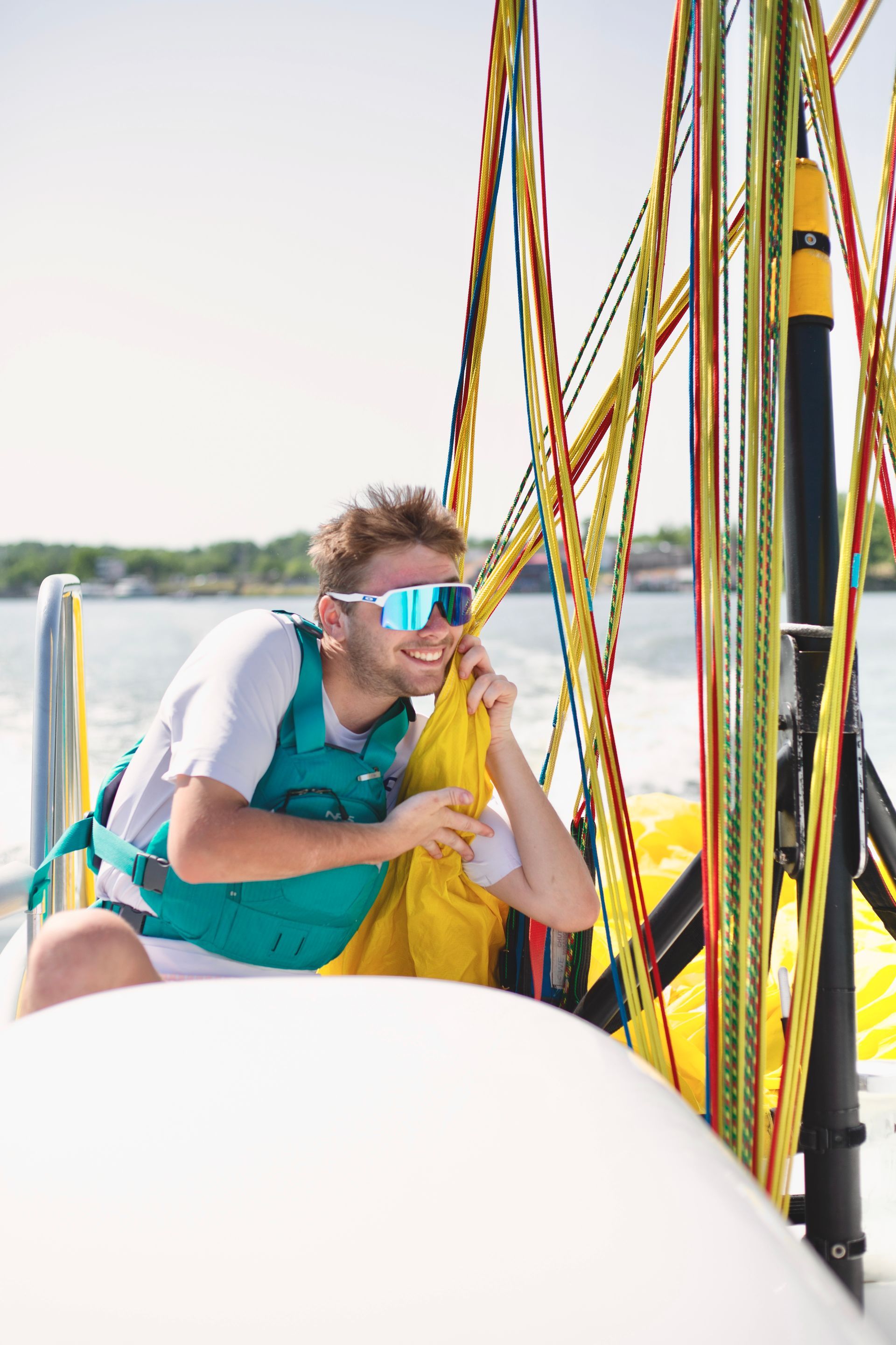 Person in sunglasses on a sailboat, holding colorful ropes on the water