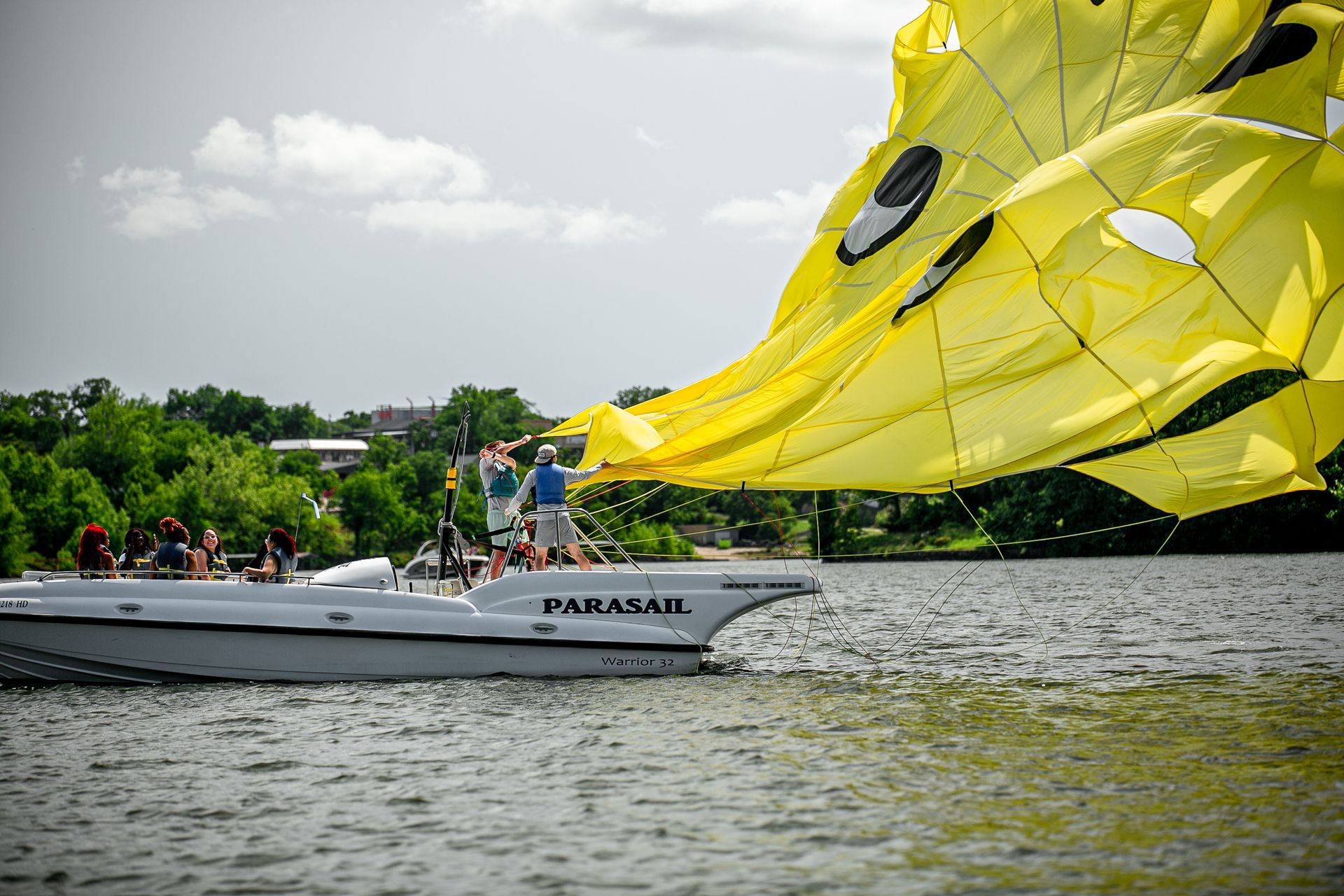 White sailboat on a lake with a large bright yellow sail, near a wooded shoreline under a cloudy sky