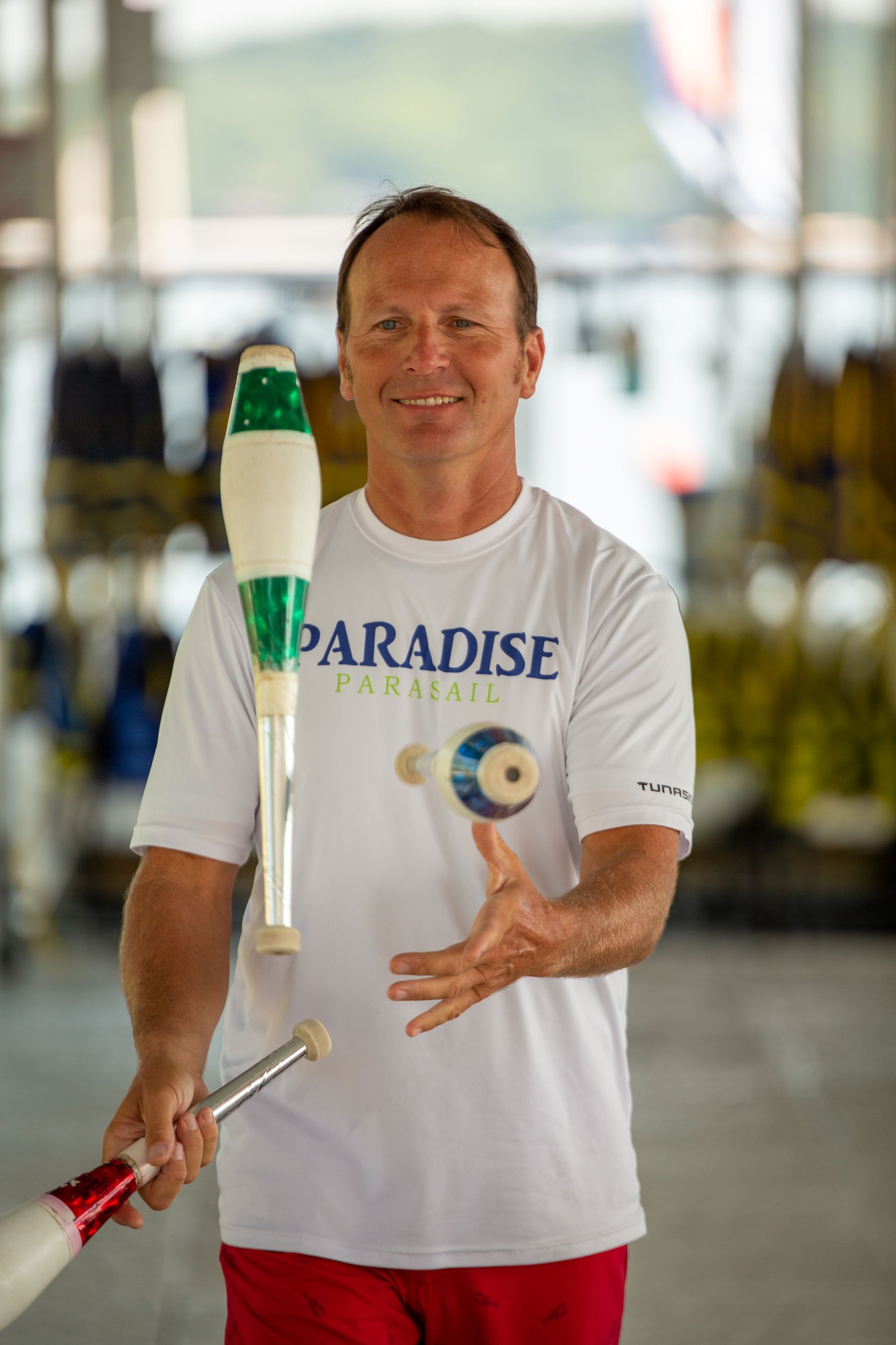 Man juggling torches indoors, smiling in a white “Paradise” T-shirt