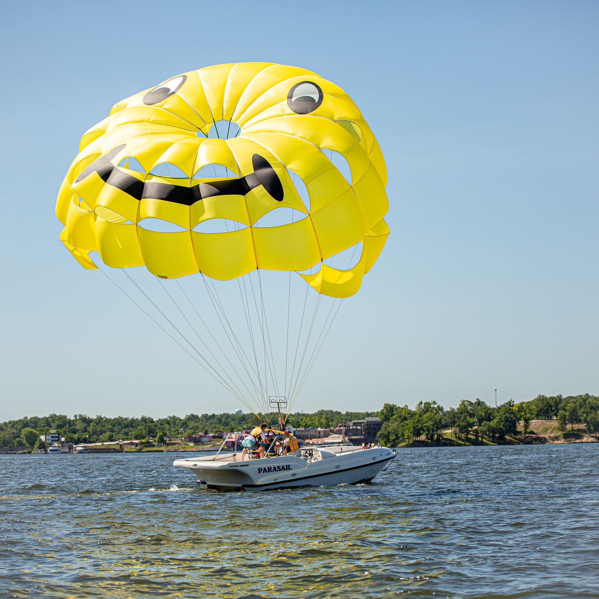 People parasailing over a lake behind a white boat with a bright yellow parachute