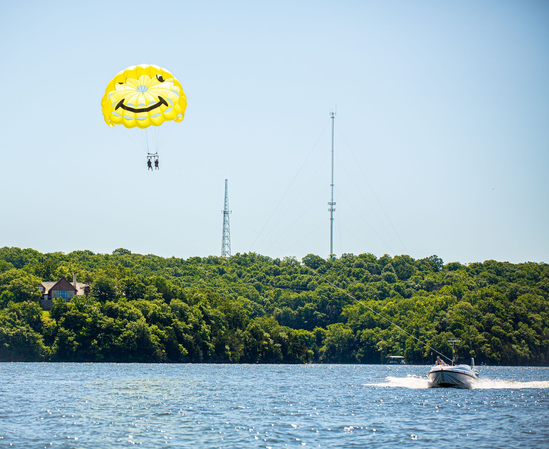 Yellow parasail over blue water near a tree-lined shore, with a small boat below.