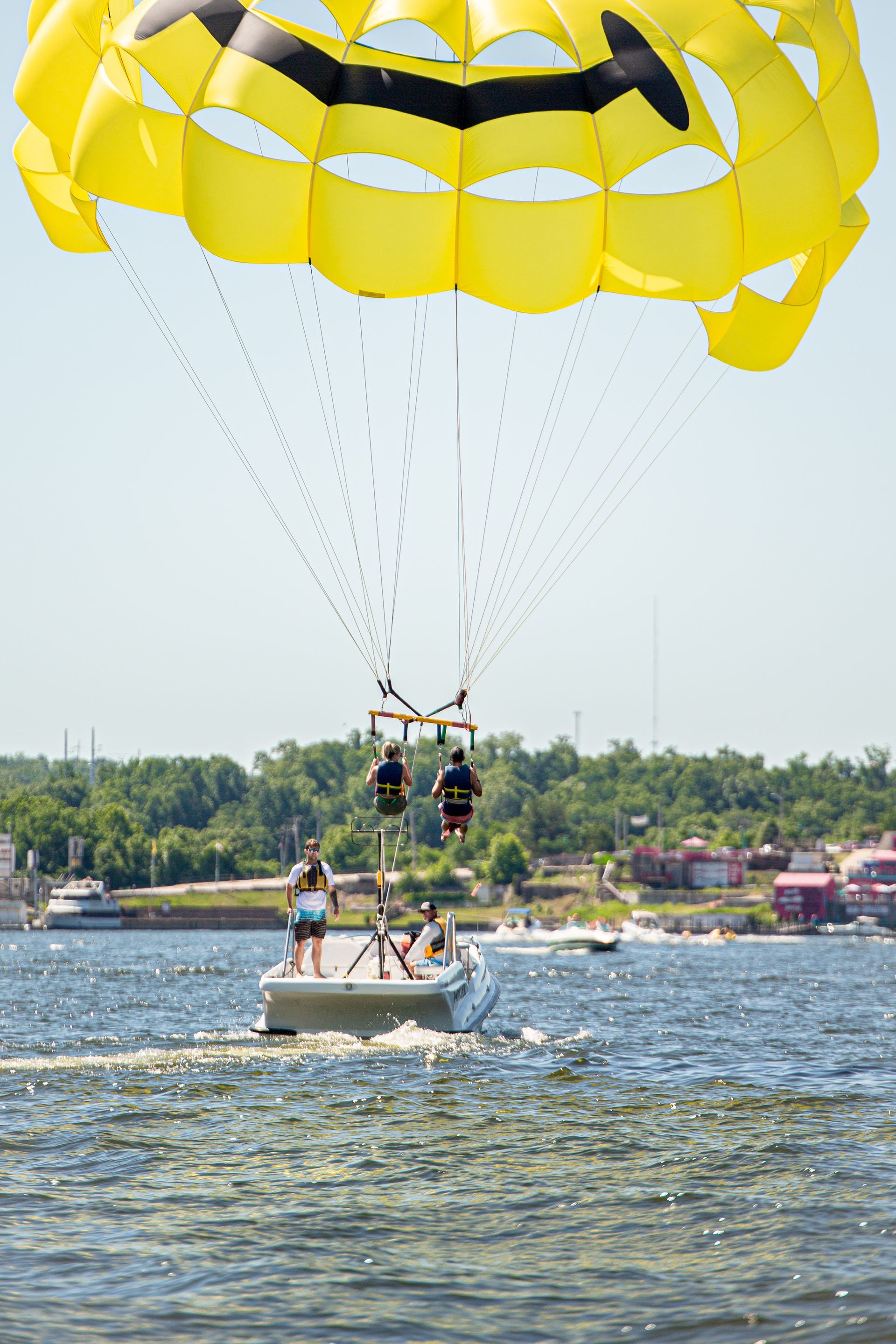 Yellow parasail towing two riders above a small boat on a lake.
