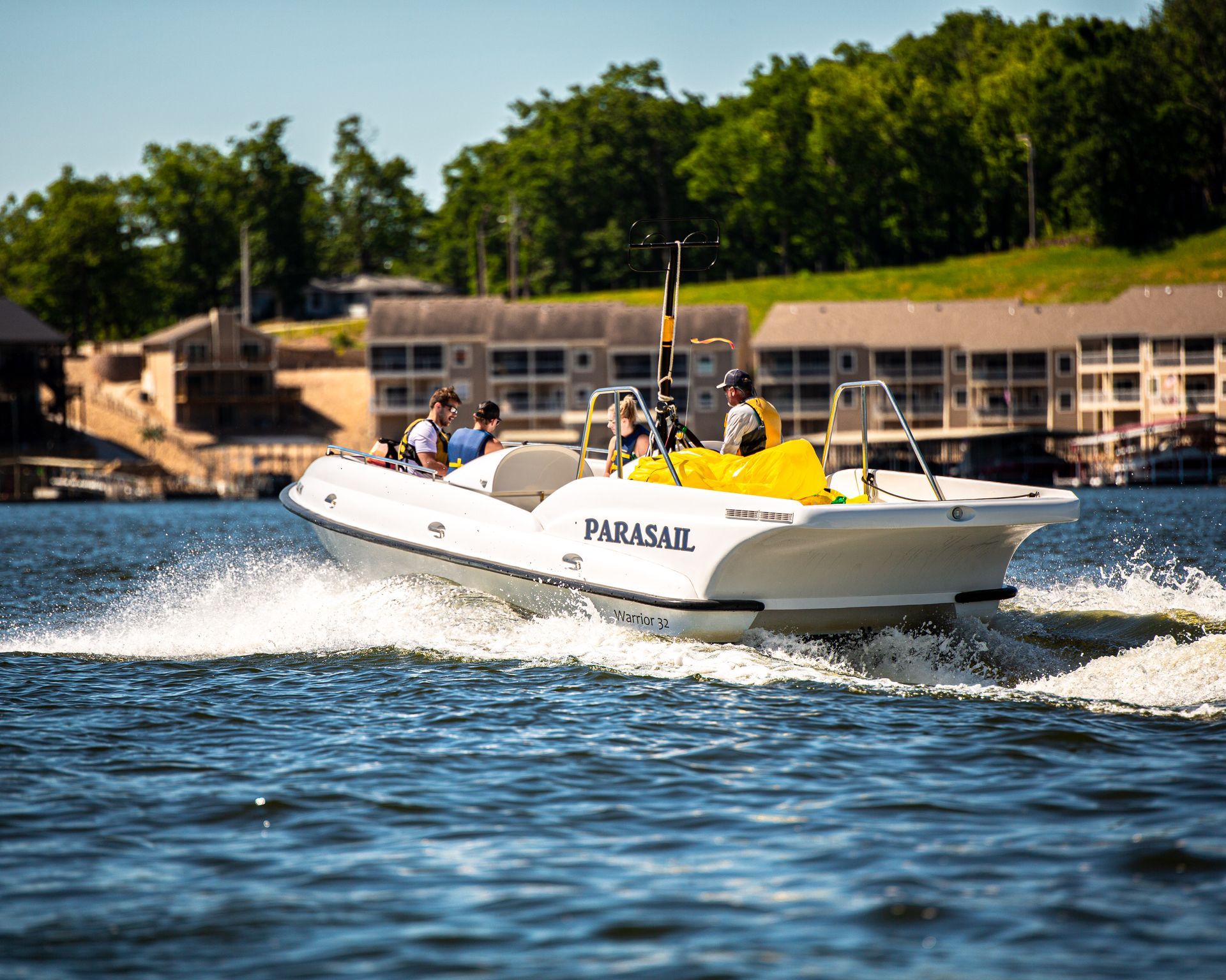White Parasail boat speeding across blue water near shoreline buildings and trees