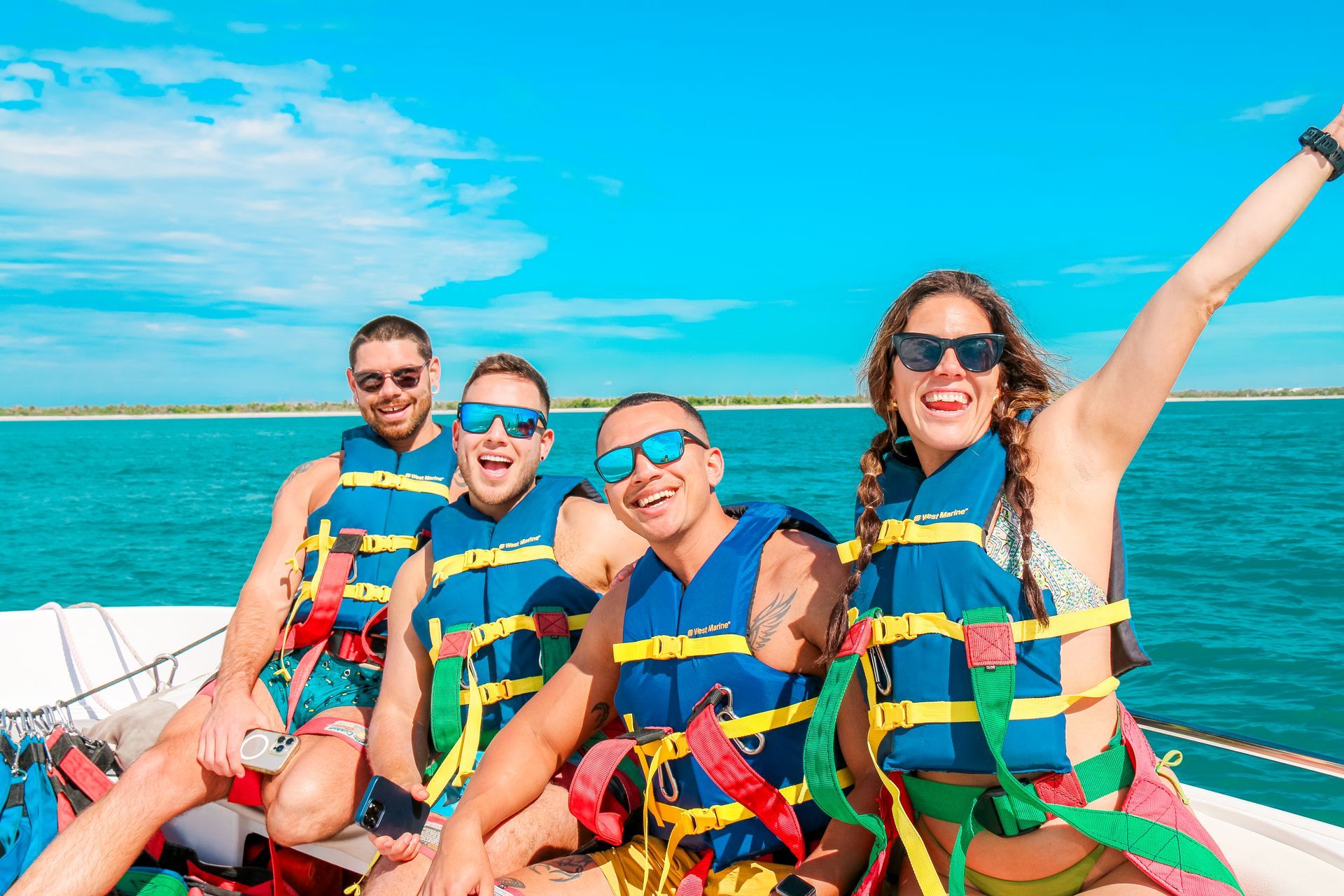 Four friends in life jackets smiling on a boat ride with bright blue water and sky