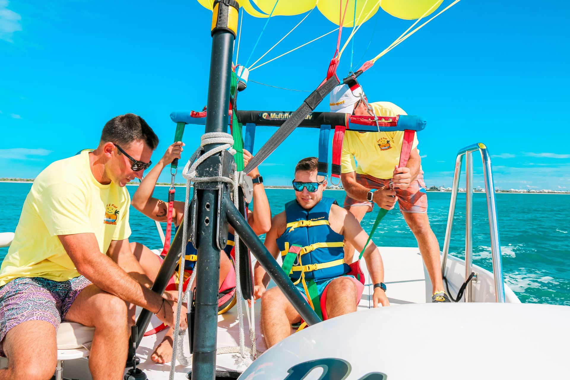 People sailing on a boat in bright sun, with turquoise water and yellow parasails overhead