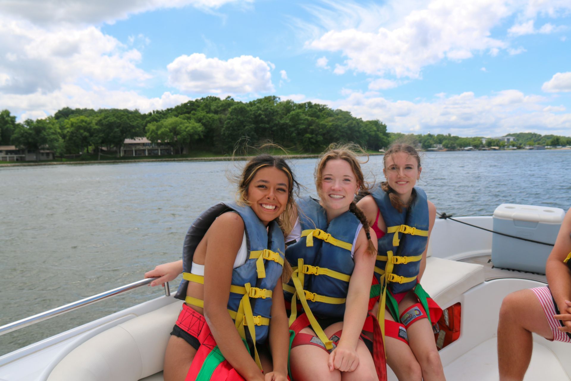 Three people in life jackets smiling on a boat on a lake under a blue sky
